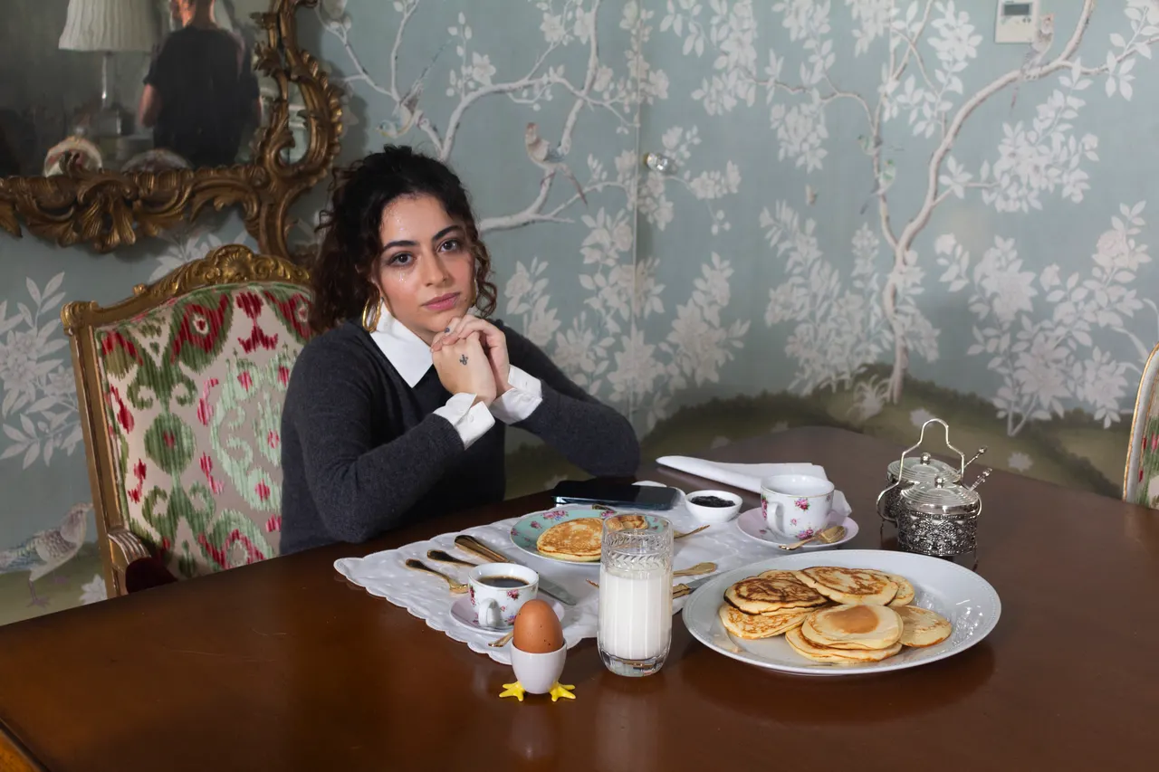 Laura de uniforme escolar à mesa de um café da manhã formal, com panquecas e leite.