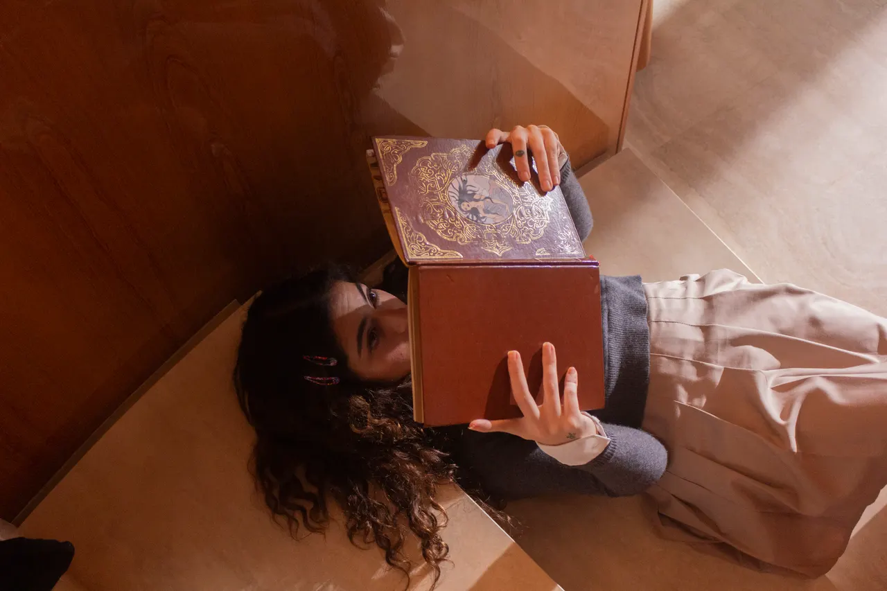 Laura deitada na escada, lendo um livro antigo de capa dourada.