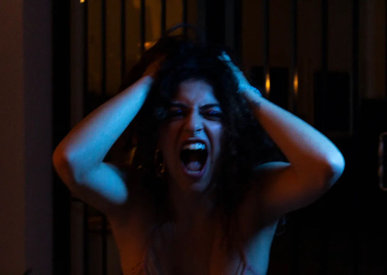 Laura grita com as mãos no cabelo, sob luz azul.