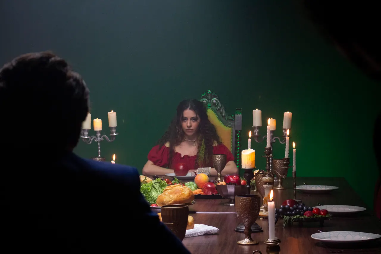 Laura à cabeceira da mesa iluminada por velas, de frente para um homem visto de costas.