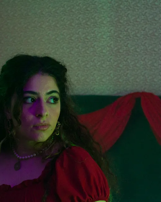 Laura, de vermelho, olha de lado, com cortinas de veludo atrás.