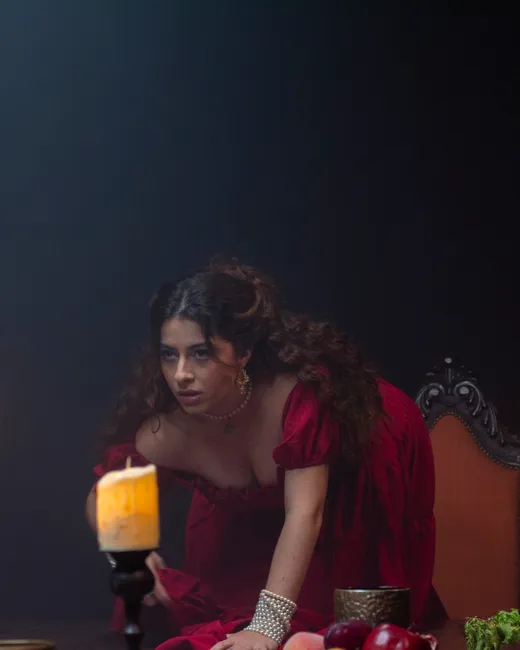 Laura, de vestido vermelho, debruçada sobre a mesa do banquete, com uma vela à frente.